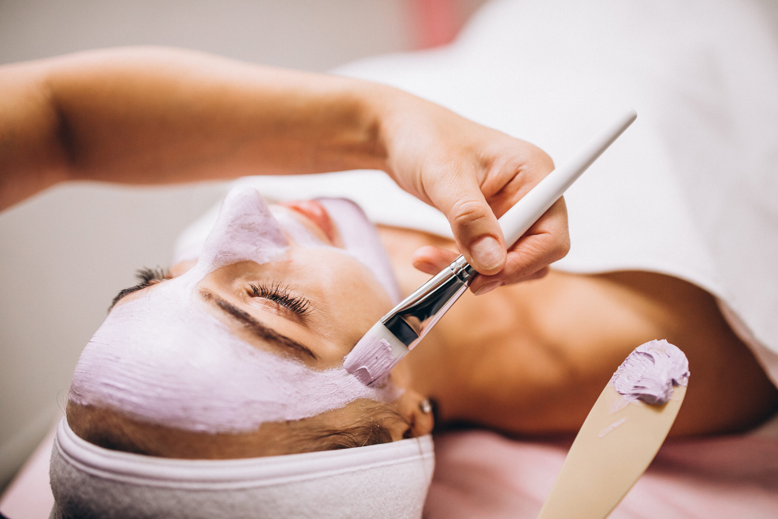 cosmetologist applying mask on a face of client in a beauty salon